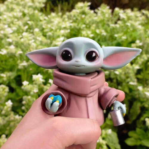 Baby Grogu Figure holding a half-eaten Nevarro Nummies on the right hand and bag on the left hand